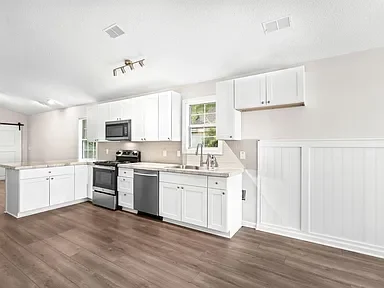 Kitchen before remodel with white cabinets, dark wood floors, and basic layout in an Outer Banks home.